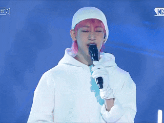 a person with pink hair is holding a microphone and giving an ok sign