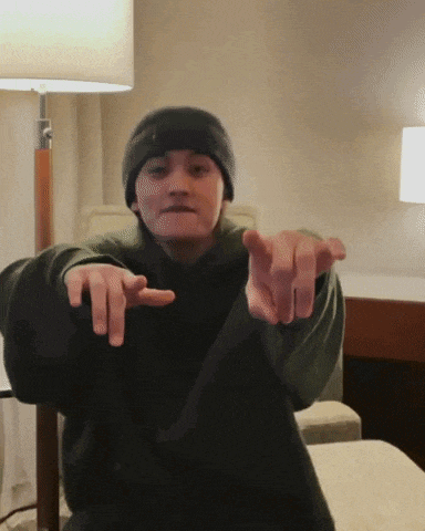 a young man wearing a beanie and a black sweater is pointing at the camera