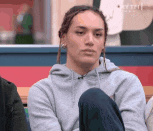 a woman in a grey hoodie is sitting down with her legs crossed and looking at the camera .
