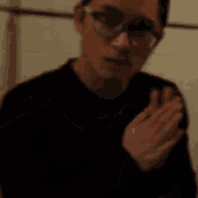 a man wearing glasses and a black shirt is holding a piece of food in his hand .
