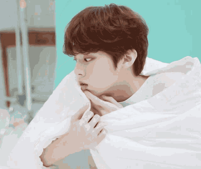 a young man is wrapped in a white blanket and biting his finger