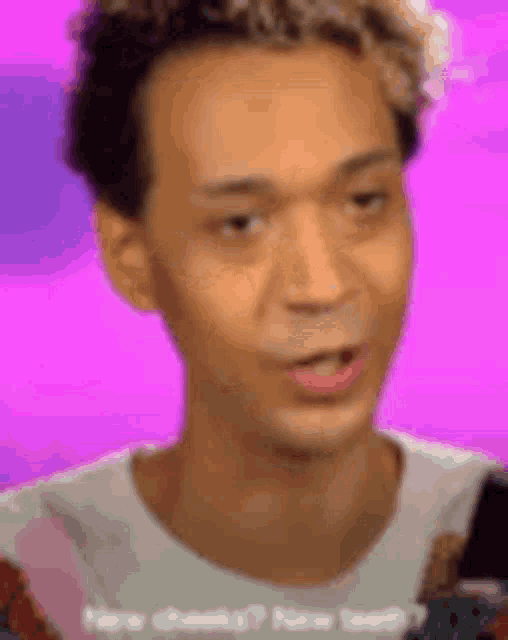 a man with curly hair is making a funny face while talking on a pink background .