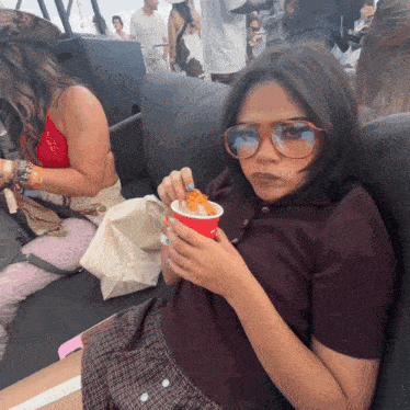 a woman wearing sunglasses holds a cup of food