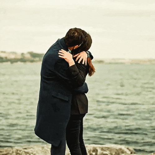 a man and a woman hugging in front of the water
