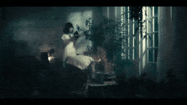 a woman in a white dress sits in front of a window