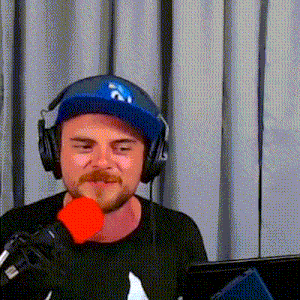 a man with a beard wearing headphones and a hat is holding a red microphone .