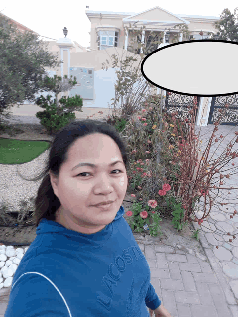 a woman wearing a blue lacoste sweatshirt is standing in front of a house