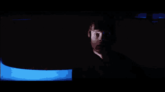 a man 's face is visible in a dark room with a blue light behind him
