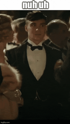 a man in a tuxedo is standing in a crowd with a caption that says " nuh uh "