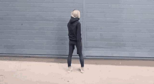 a woman wearing a black hoodie and jeans stands in front of a blue wall