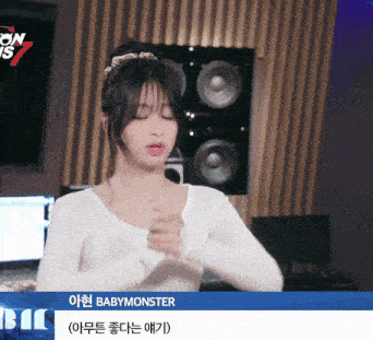 a woman in a white shirt is standing in front of a sign that says " babymonster "