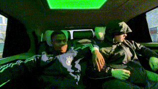 two men are sitting in the back seat of a car with a green light on the ceiling