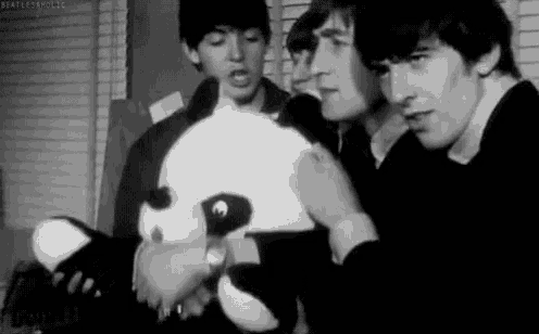 a black and white photo of the beatles holding a stuffed panda .