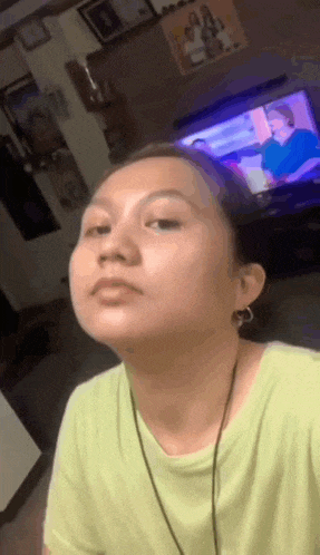a woman in a green shirt is making a funny face while sitting in front of a television .