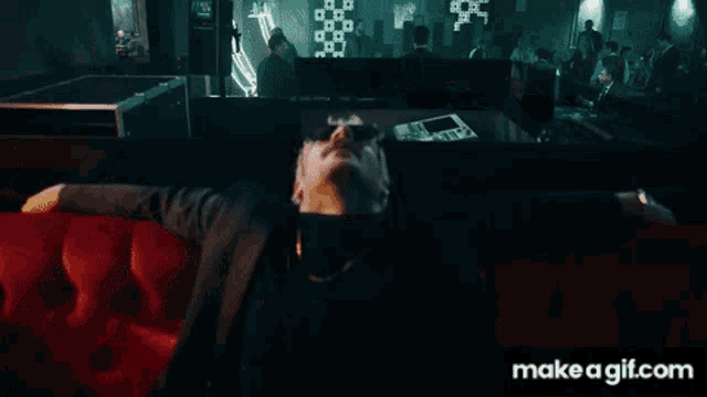 a man is sitting on a red couch with his arms outstretched in front of a make a gif.com screen