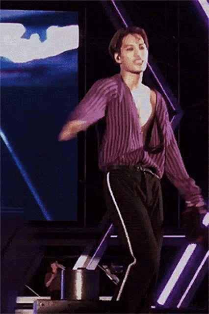 a man in a striped shirt is standing on a stage with his arms outstretched