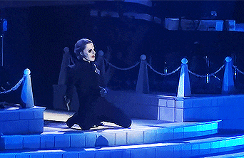 a woman in a black dress is kneeling down on a stage