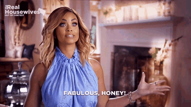 a woman in a blue dress says fabulous honey in front of a fireplace