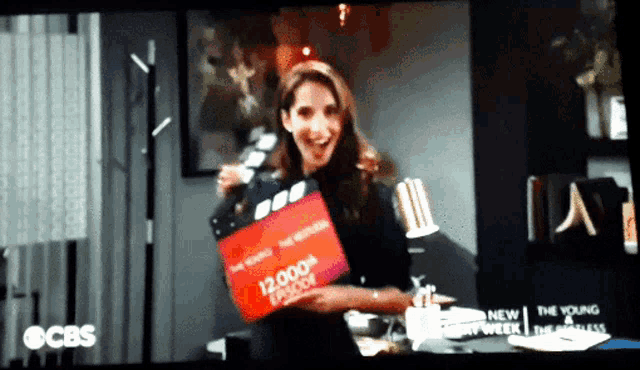a woman holding a 12,000th episode clapper board