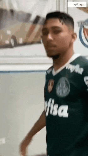 a man in a green soccer jersey is standing in a room .