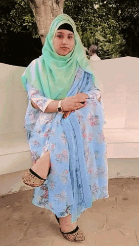 a woman wearing a hijab sits on a bench with her legs crossed