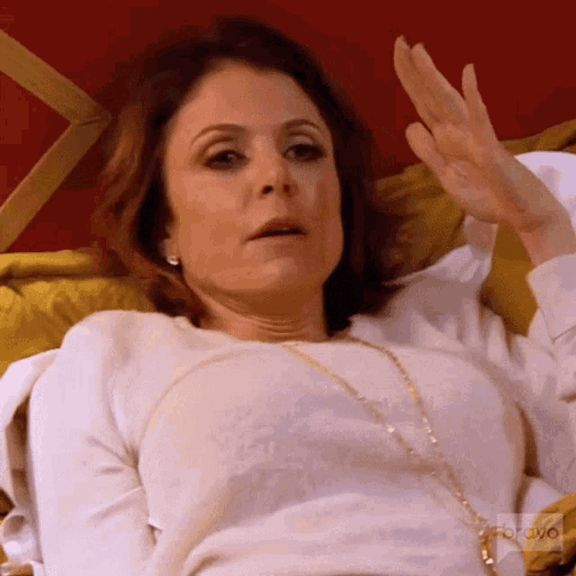 a woman in a white shirt is laying on a bed with her hand up .
