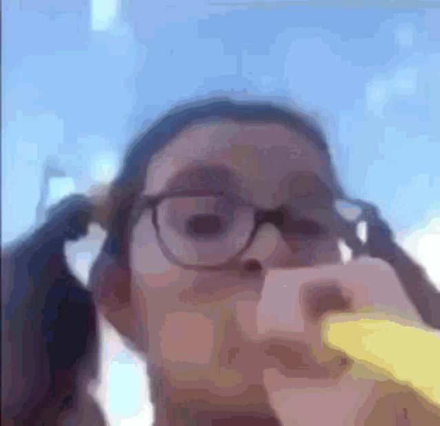 a person wearing glasses is holding a banana in front of their face .