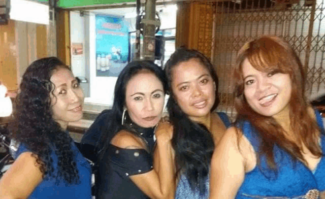 a group of four women are posing for a picture together in front of a building .