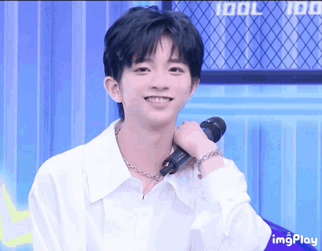 a young man in a white shirt is smiling while holding a microphone in front of a sign that says idol 100