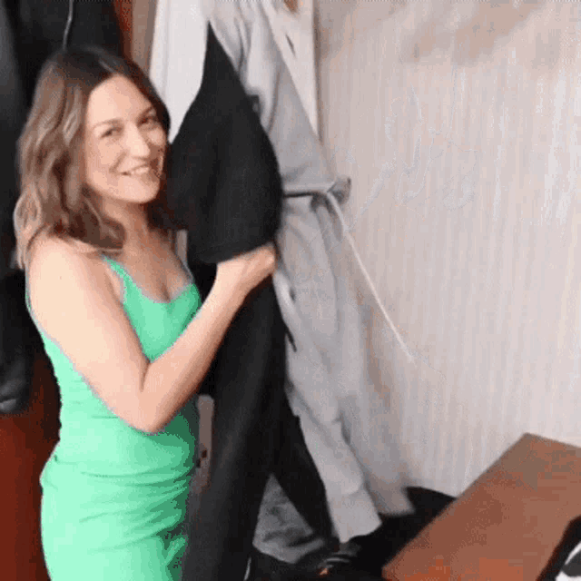 a woman in a green dress is smiling while holding a black jacket