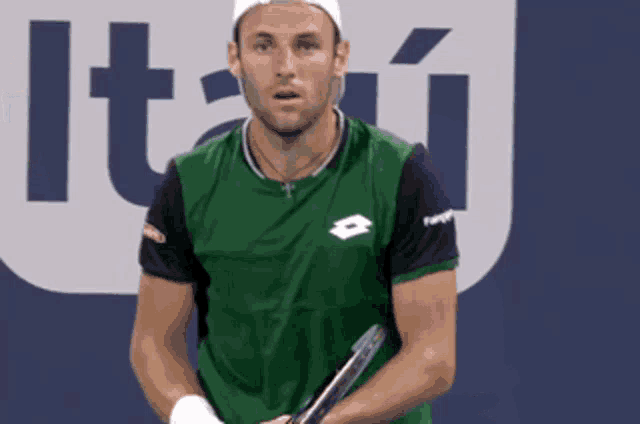 a man is holding a tennis racket in front of a sign that says itai