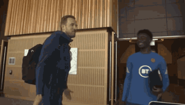 a man wearing a blue bt shirt is talking to another man