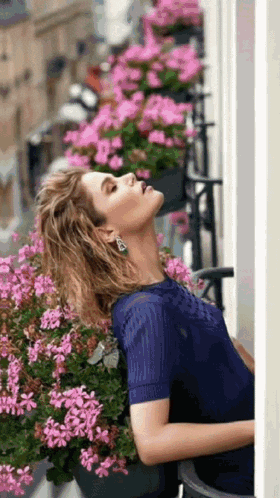 a woman in a blue dress is leaning against a wall surrounded by flowers .
