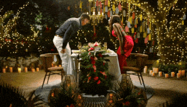 a man and woman sit at a table with candles and flowers