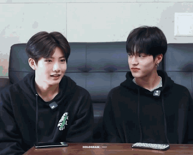 two young boys are sitting next to each other and the word hologram is on the table