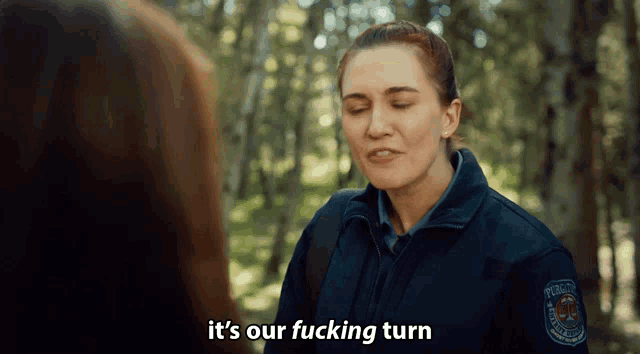 a woman in a police uniform says it 's our fucking turn in front of a forest