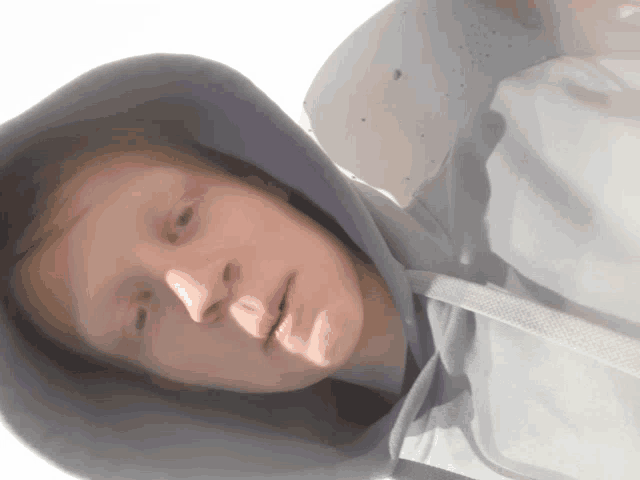 a young man wearing a hooded sweatshirt looks down at the camera