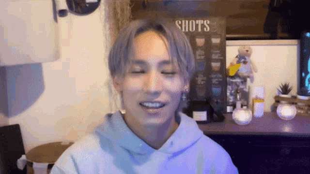 a man in a purple hoodie is smiling in front of a sign that says shots