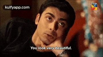 a man is sitting at a table with his hand on his chin and says `` you look very beautiful '' .