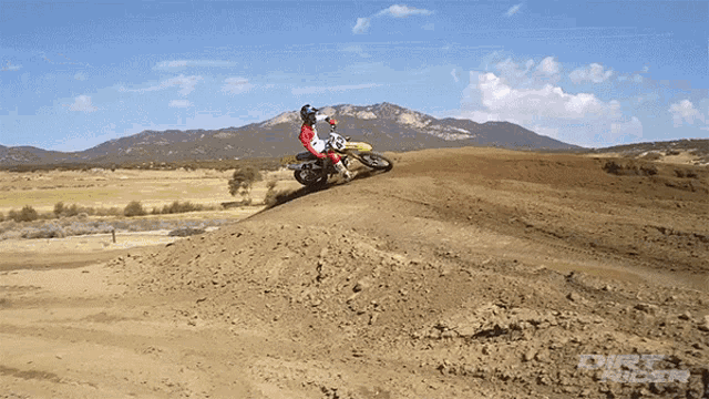 a person riding a dirt bike on a dirt road with mountains in the background