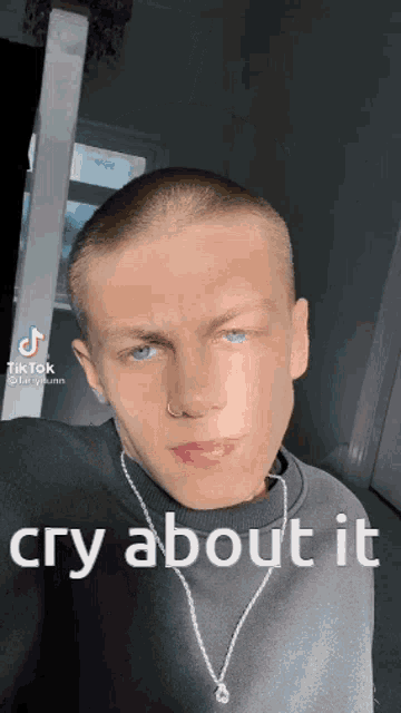 a young man with a shaved head and blue eyes is wearing a necklace and a sweater .