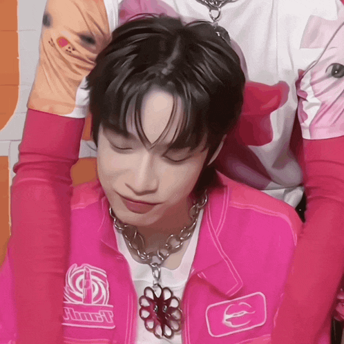 a young man wearing a pink jacket with a necklace that says just