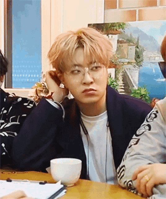 a young man wearing glasses is sitting at a table with a cup of coffee