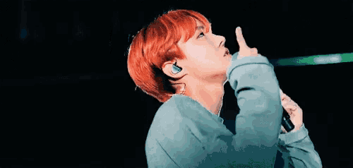 a man with red hair is holding a microphone in his hand and pointing upwards .