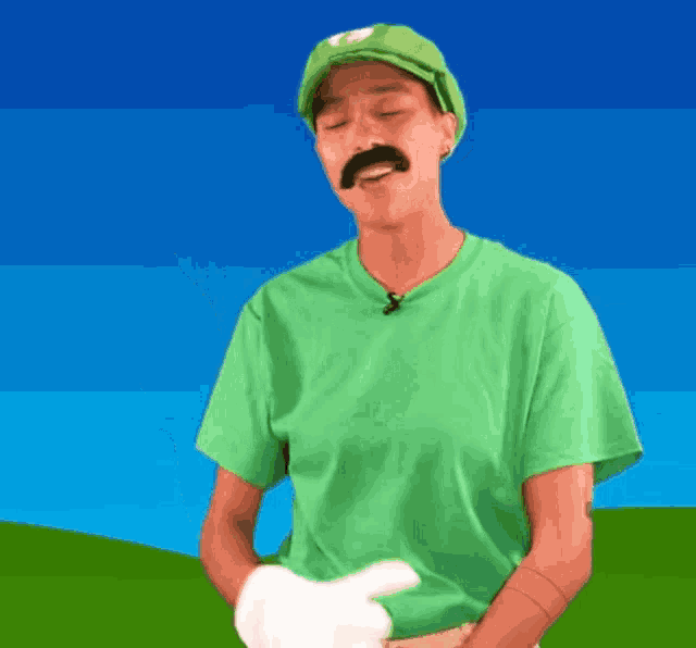 a man in a green shirt with a hat and mustache is pointing