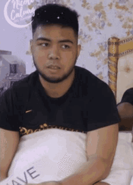 a man in a black shirt is laying on a bed with a pillow that says wave
