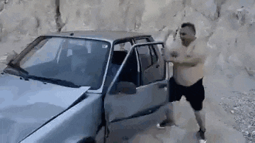 a man is standing next to a broken car on a dirt road .