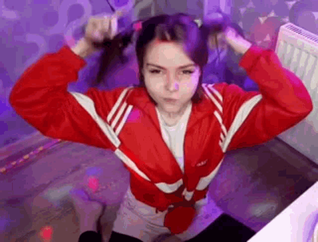 a girl in a red jacket is sitting on the floor holding her hair .