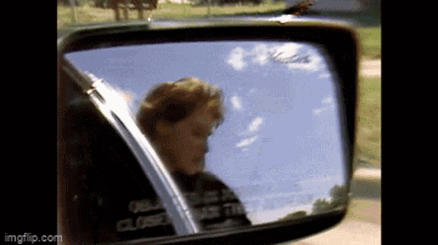 a rear view mirror of a car shows a person looking out the window