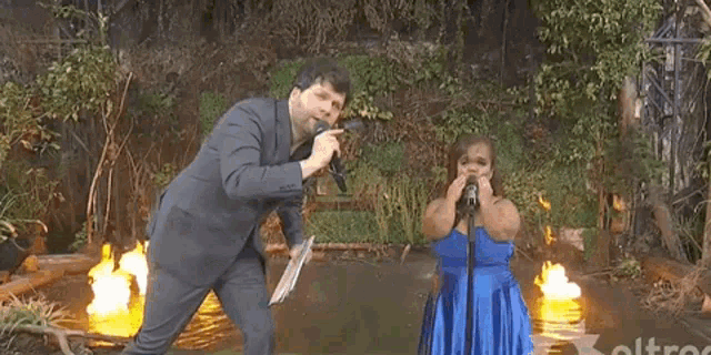 a man in a suit and a woman in a blue dress are singing in front of a fire and the words pone la musica
